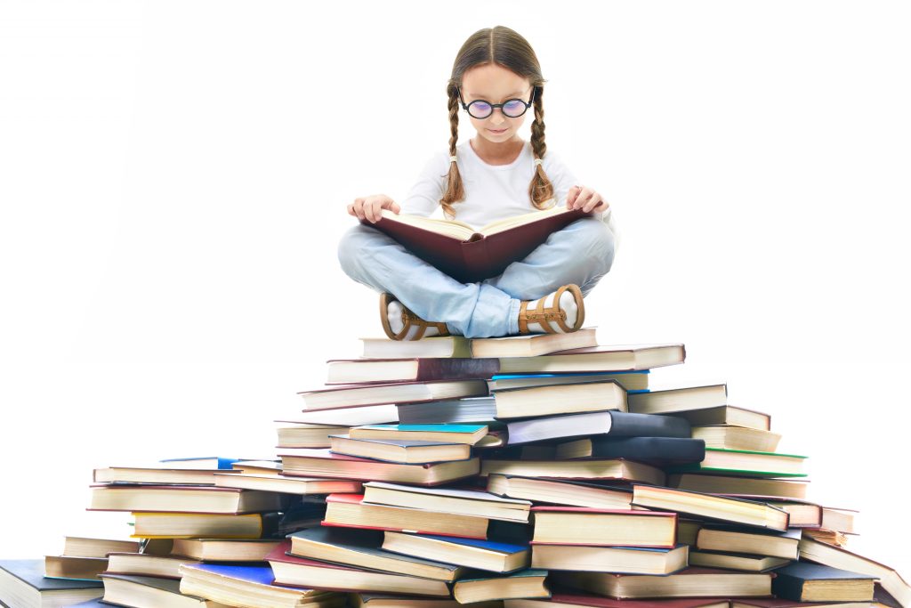 Kid sitting on a pile of books reading