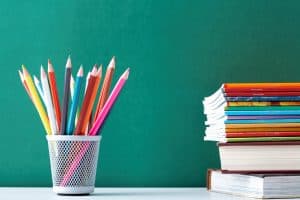 Pencils and books sitting on desk in front of chalkboard