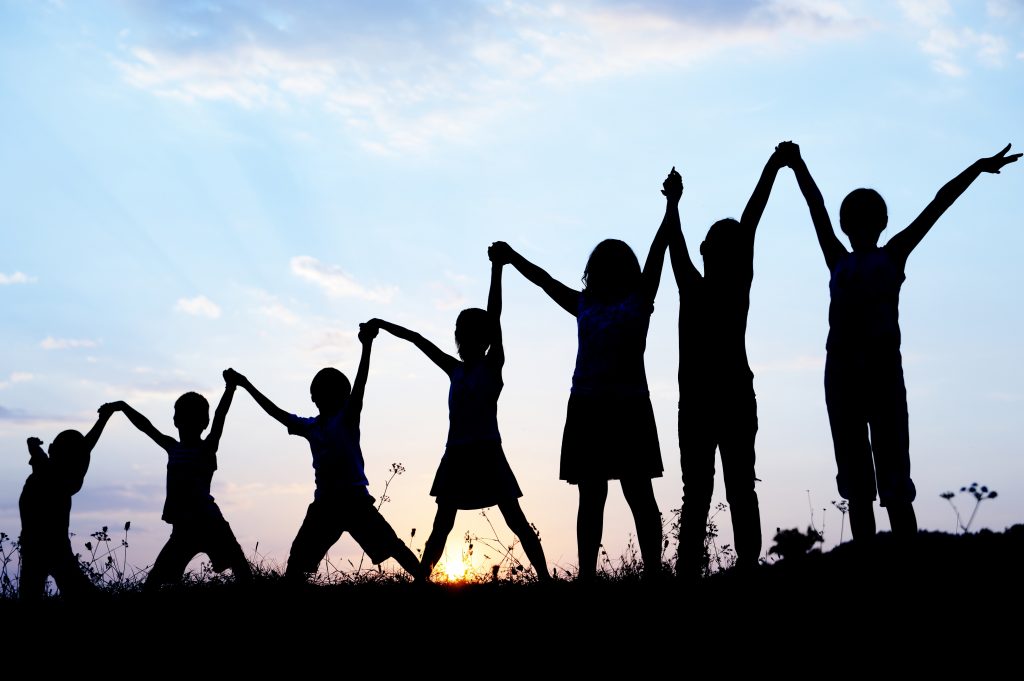 Kids holding hands with arms raised at sunset