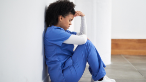 Health care professional sitting on floor holding head.